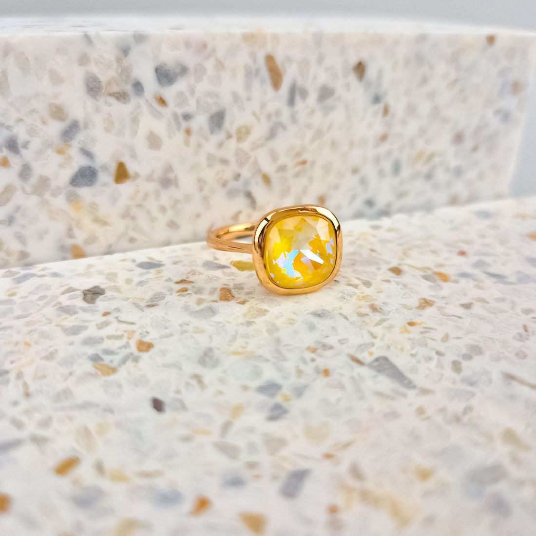 Close-up of a gold-tone ring with a sparkling yellow crystal on speckled stone