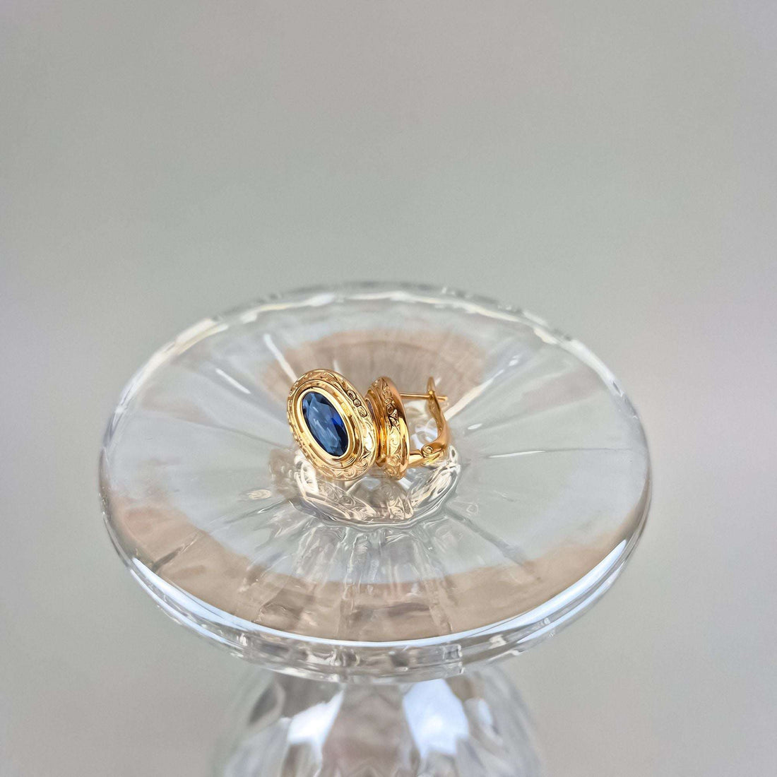 Earrings in side view on a crystal dish, leverback and blue stone visible