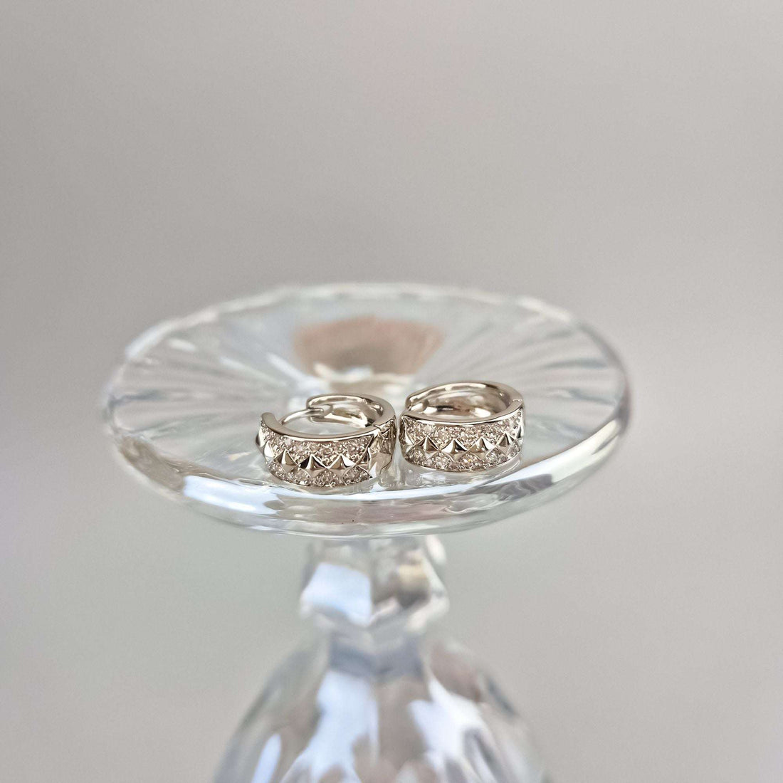 Patterned hoop earrings with cubic zirconia on a clear glass dish