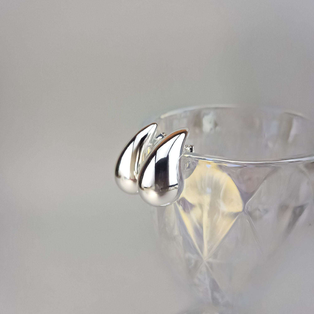 Shiny silver-tone teardrop earrings close up on the rim of a glass dish