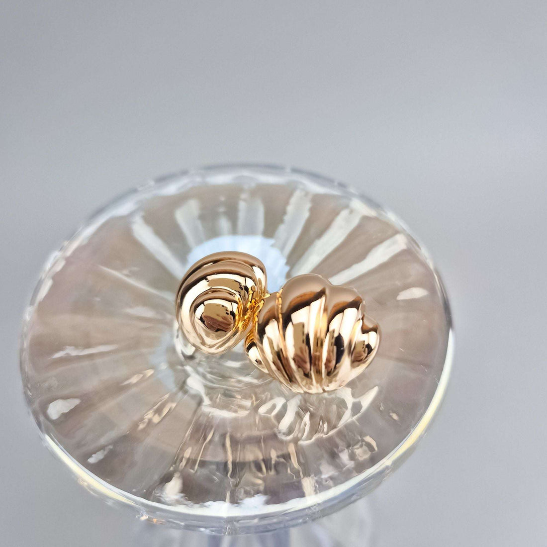 Gold-plated seashell earrings close up on a crystal glass, wavy relief visible