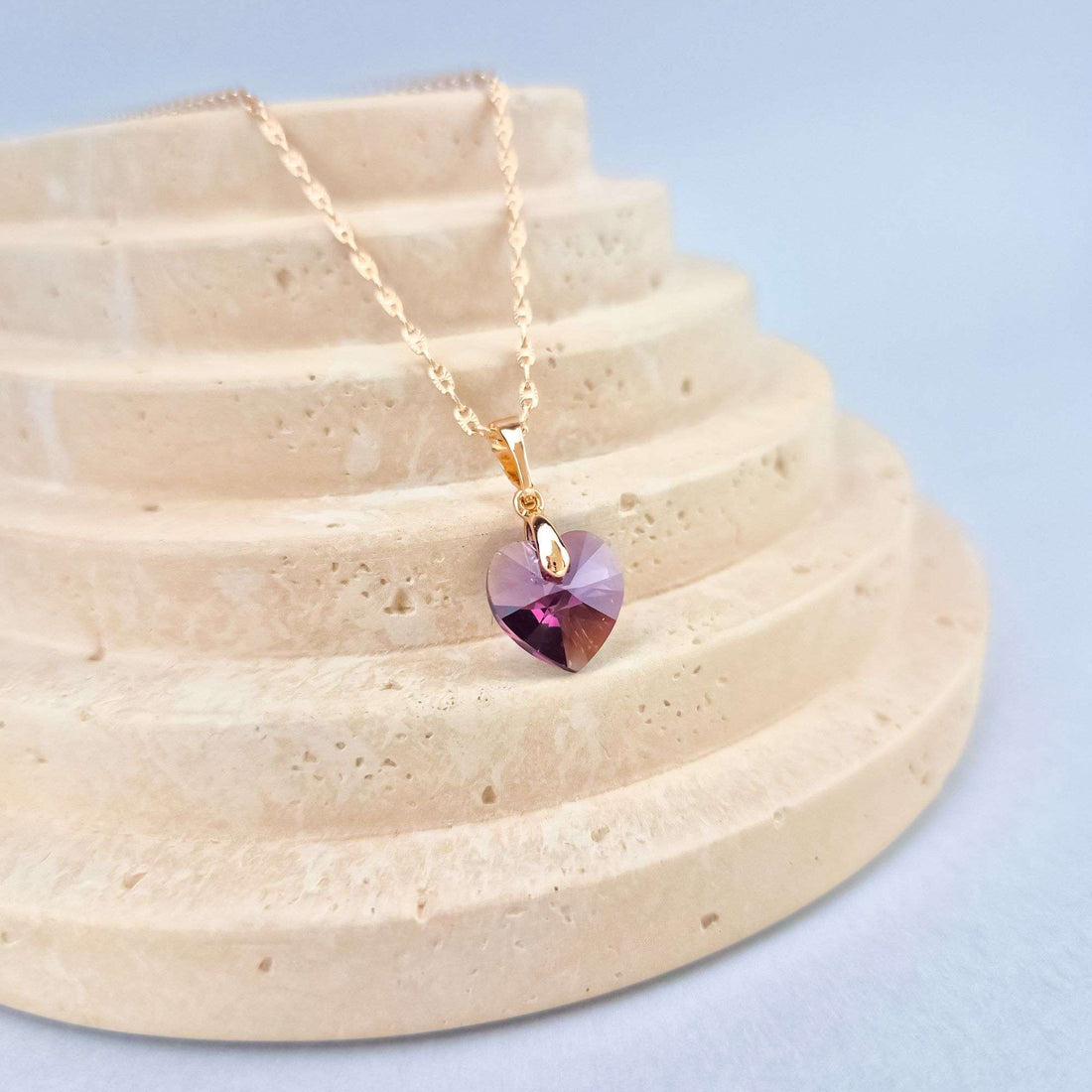Violet-pink heart crystal on a pale travertine stand, close-up
