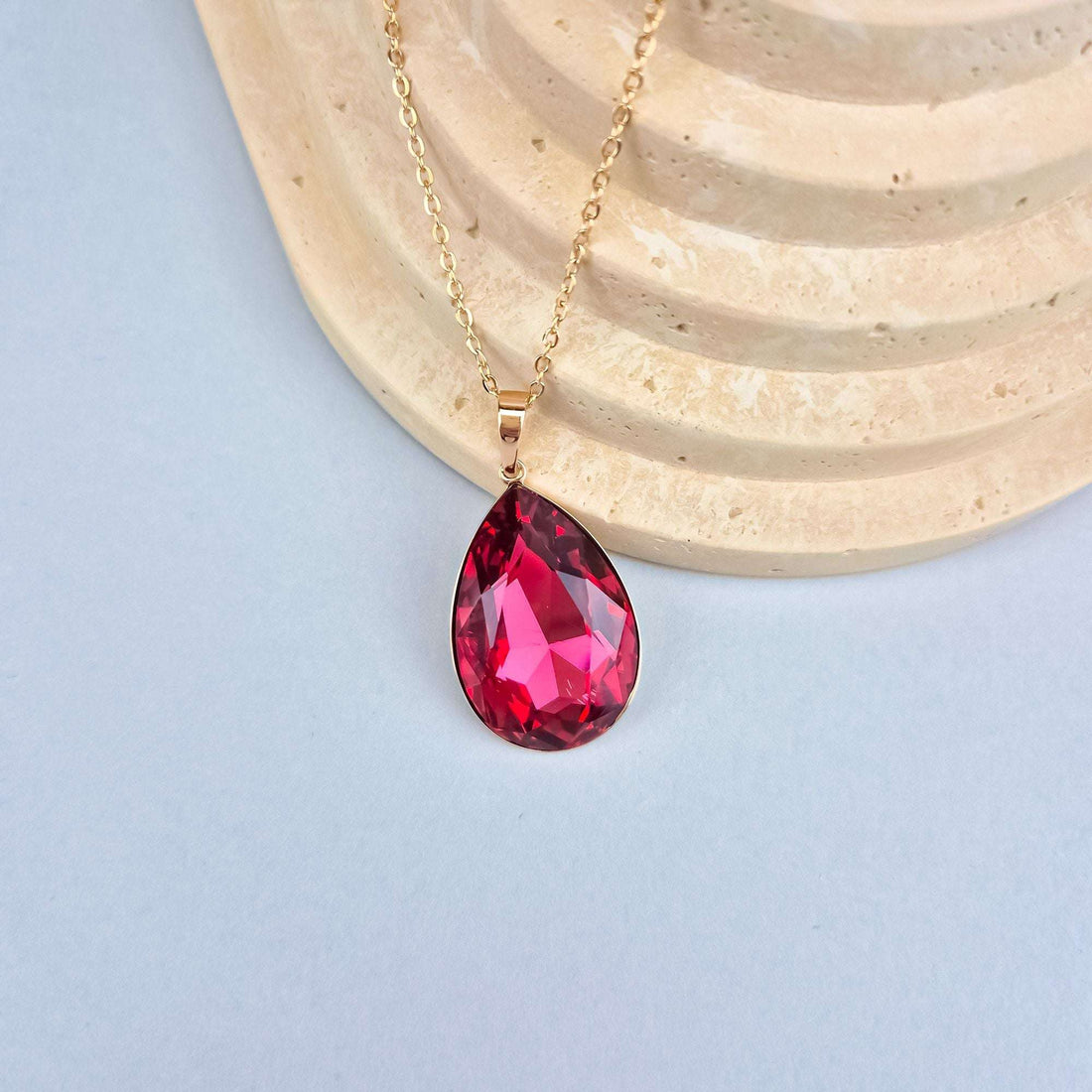 Close-up of the red crystal pendant with gold-plated chain on light stone
