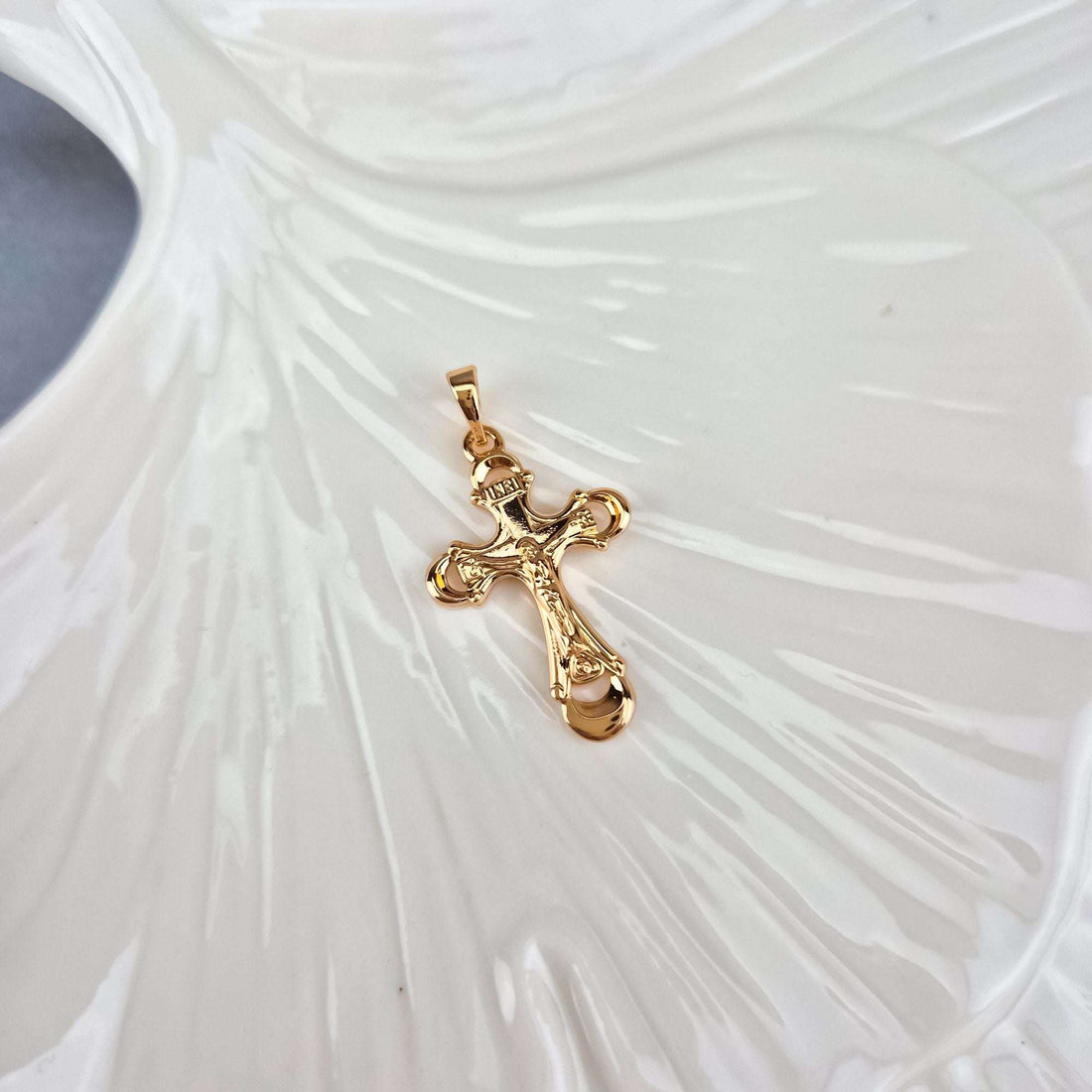 Catholic cross pendant at an angle on a white ceramic leaf, warm gold shine