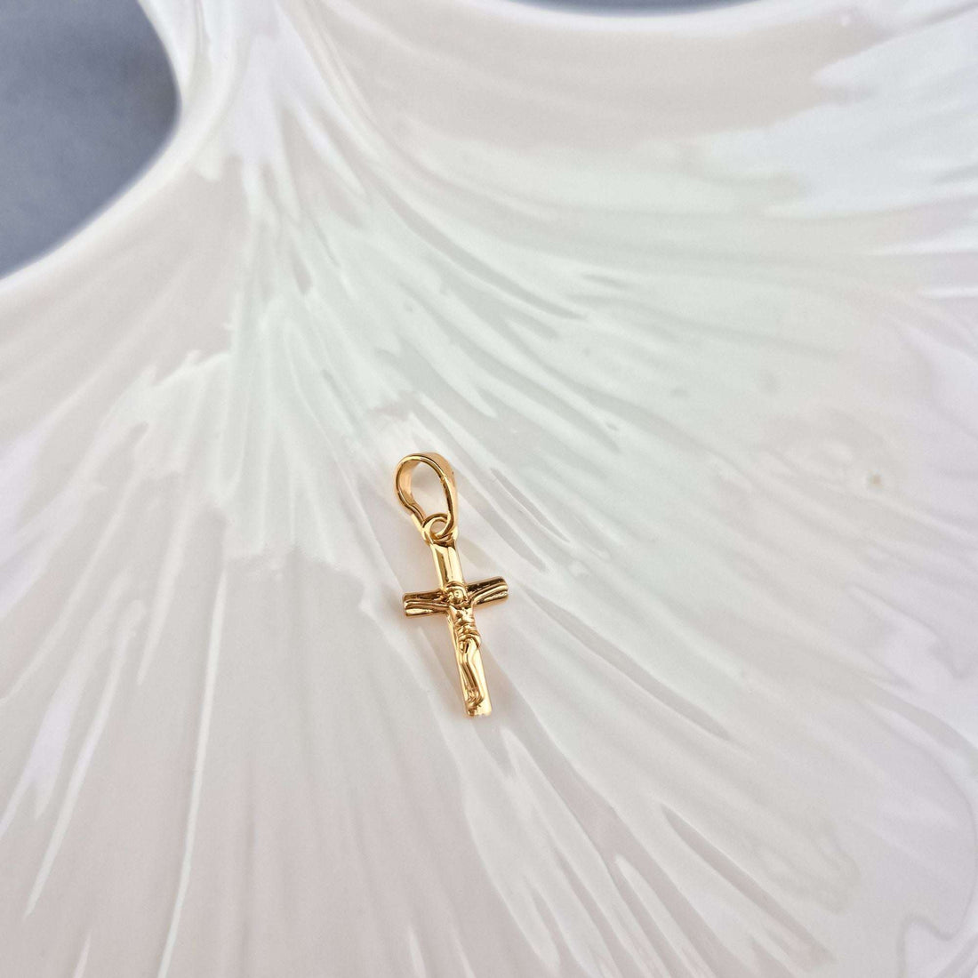 Gold-tone cross pendant with a round loop on a white ceramic leaf