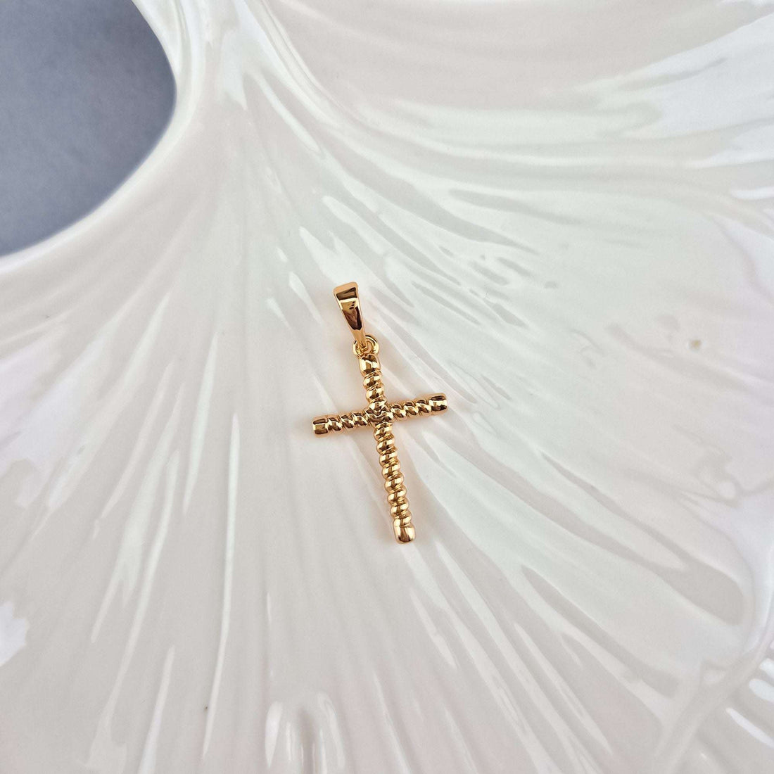 Twisted cross pendant on a white ceramic leaf, shiny gold-plated surface