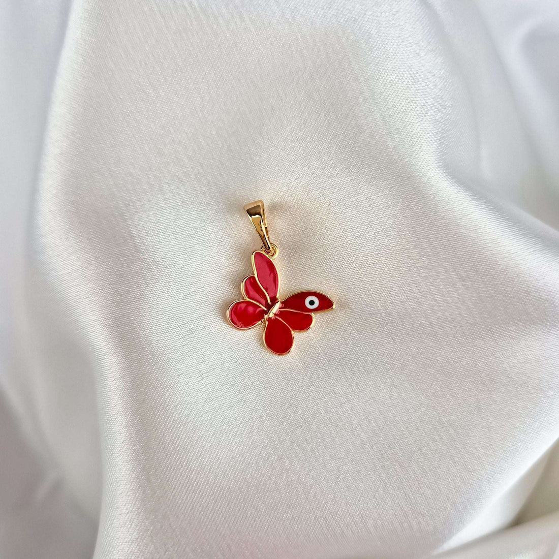 Red butterfly pendant with gold plating in close-up on white silk