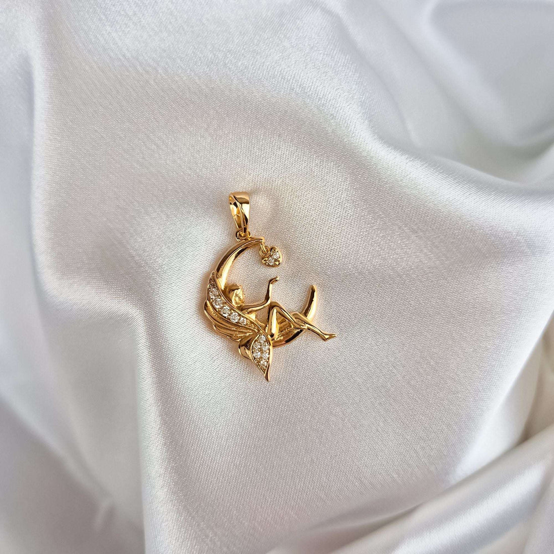 Gold-plated fairy pendant on white satin, close-up of the stone-set wings and crescent