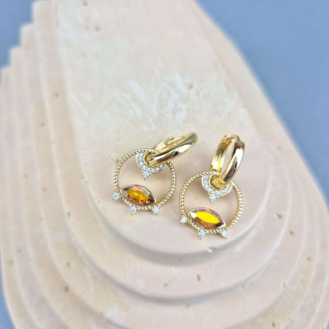 Pair of earrings with yellow marquise stones and cubic zirconia on a beige stand