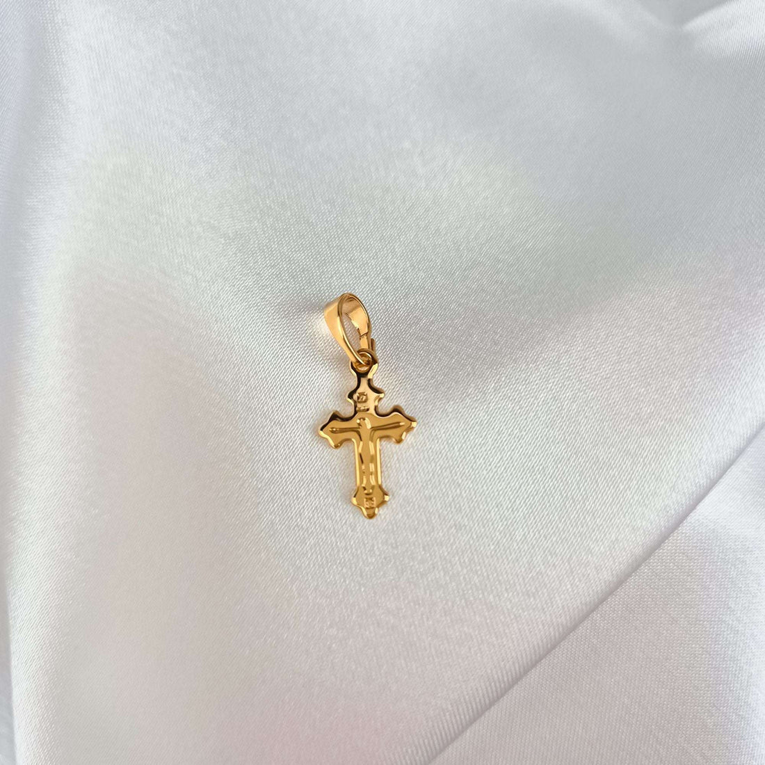 Delicate gold-plated crucifix with a relief figure on white satin