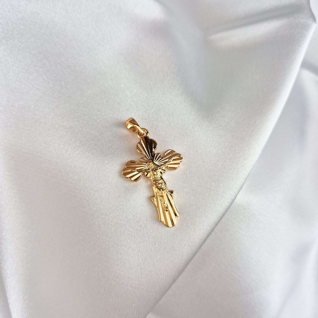 Gold-plated cross with engraved rays and the figure of Christ on white satin