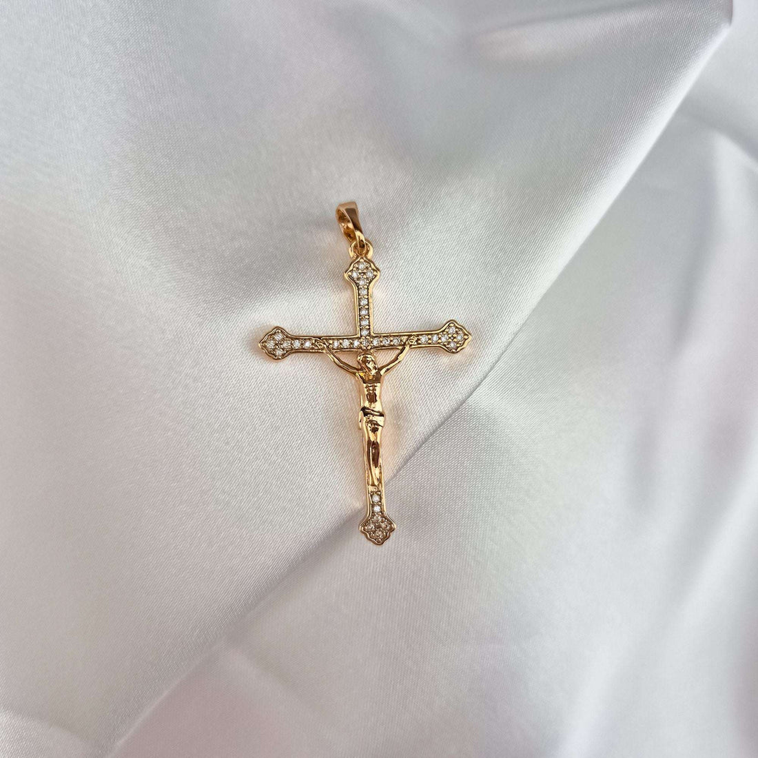Gold-plated cross set with cubic zirconia on folds of white satin