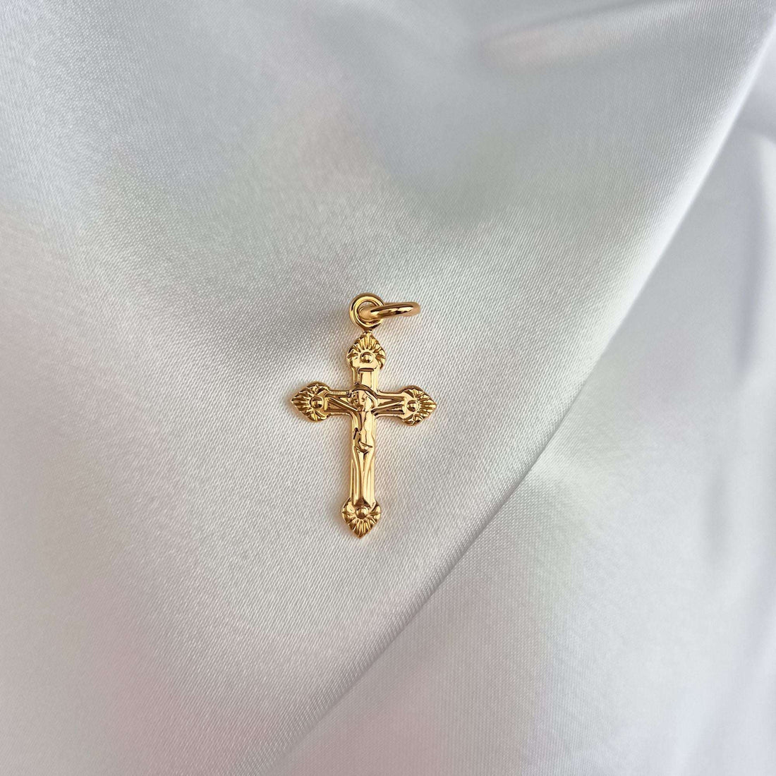 Small gold-plated cross with a round jump ring on white silk