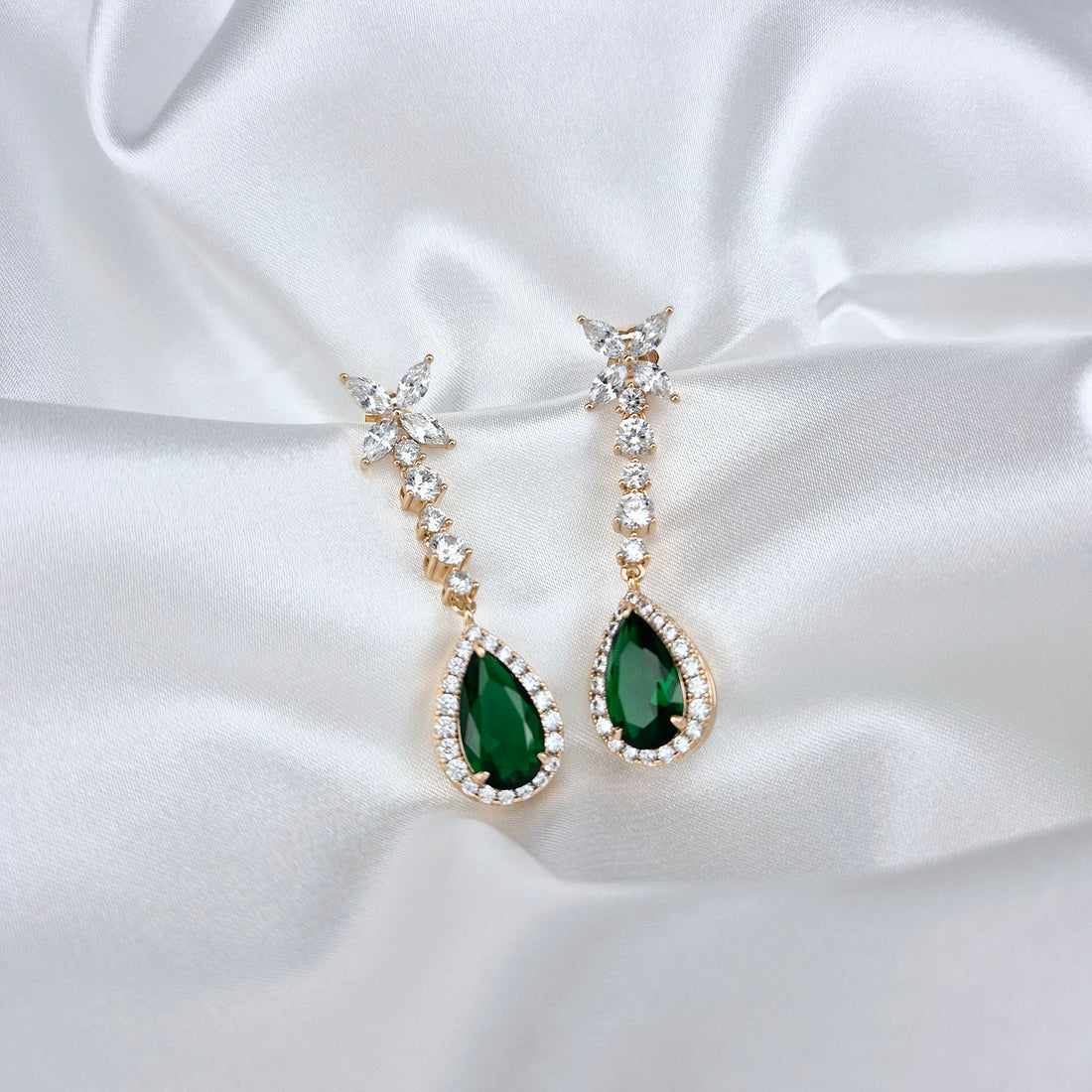 Green teardrop earrings lying on white satin