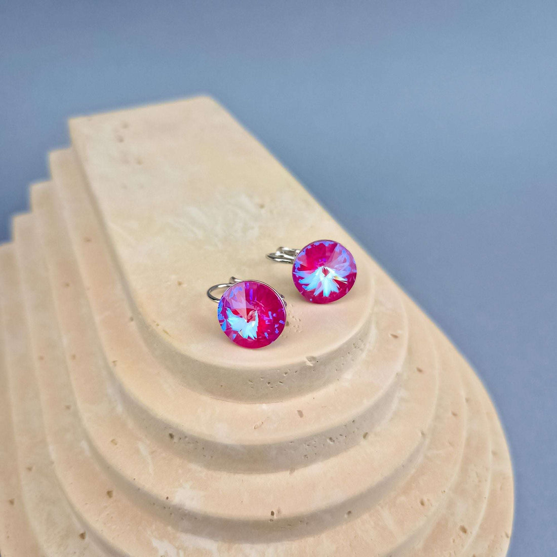 Rosy sparkling round crystal earrings with silver-tone hooks on a travertine slab