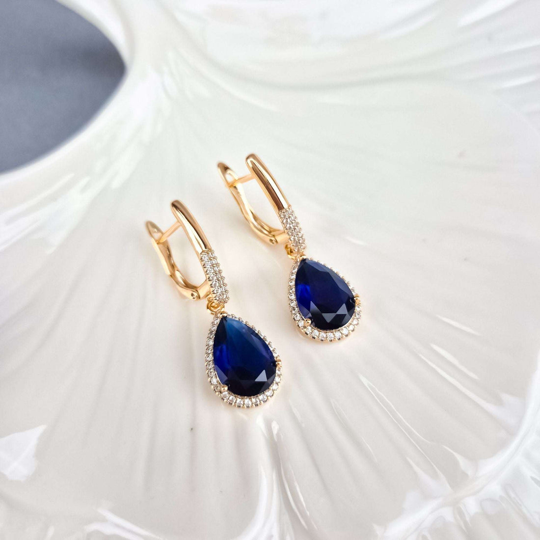 Blue cubic zirconia earrings with gold-plated leverbacks on a glossy white dish