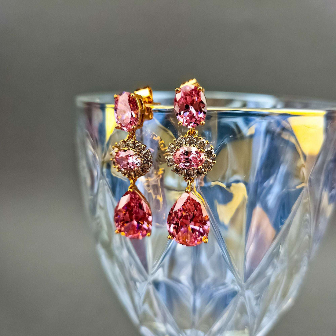 Pink crystal earrings beside a cut-glass tumbler, teardrop stone and push-back visible