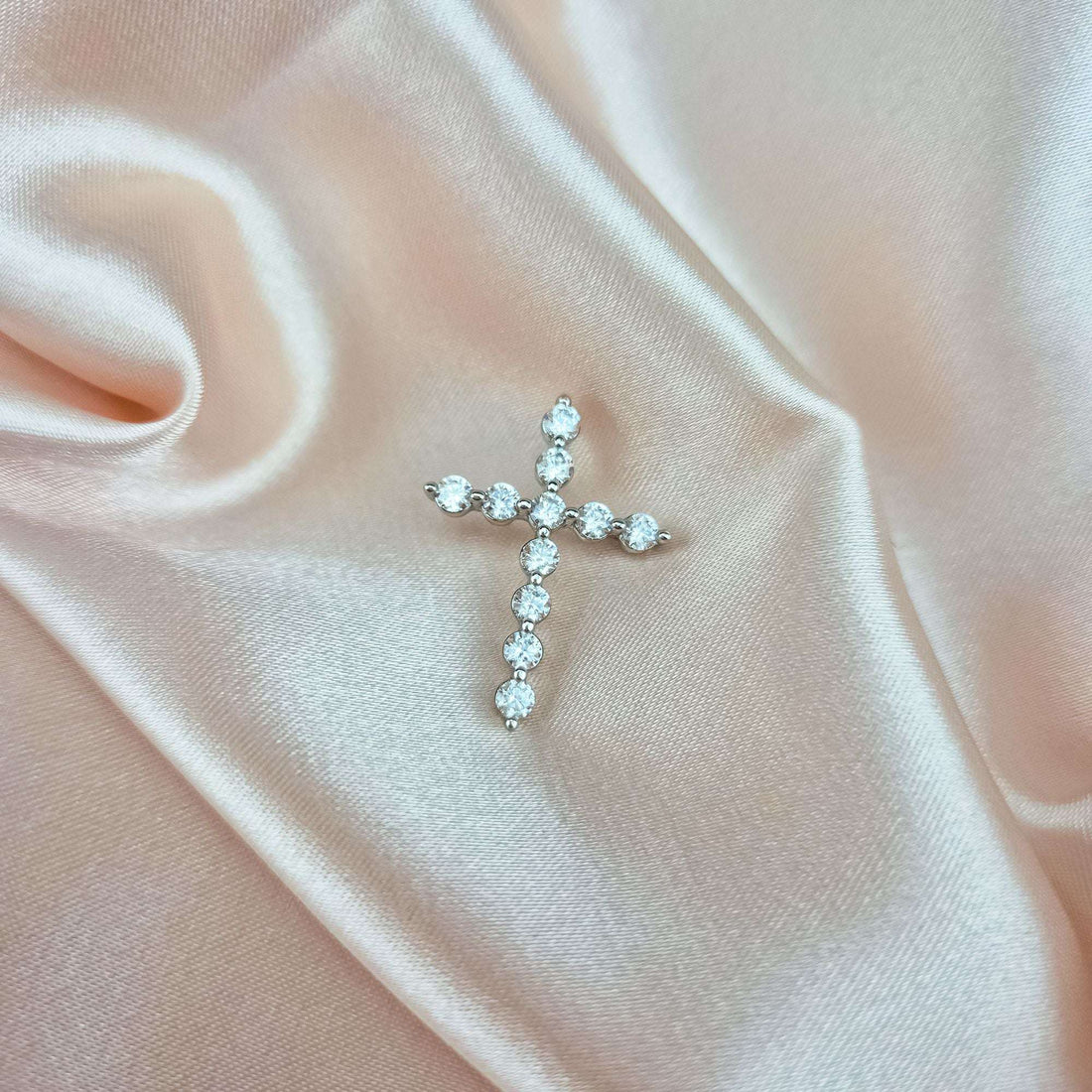 Platinum-plated cross pendant with cubic zirconia on soft peach silk