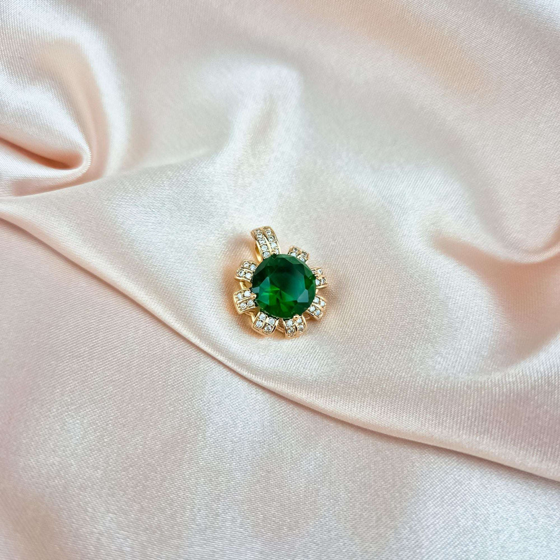Gold-tone pendant with green stone on pale pink satin