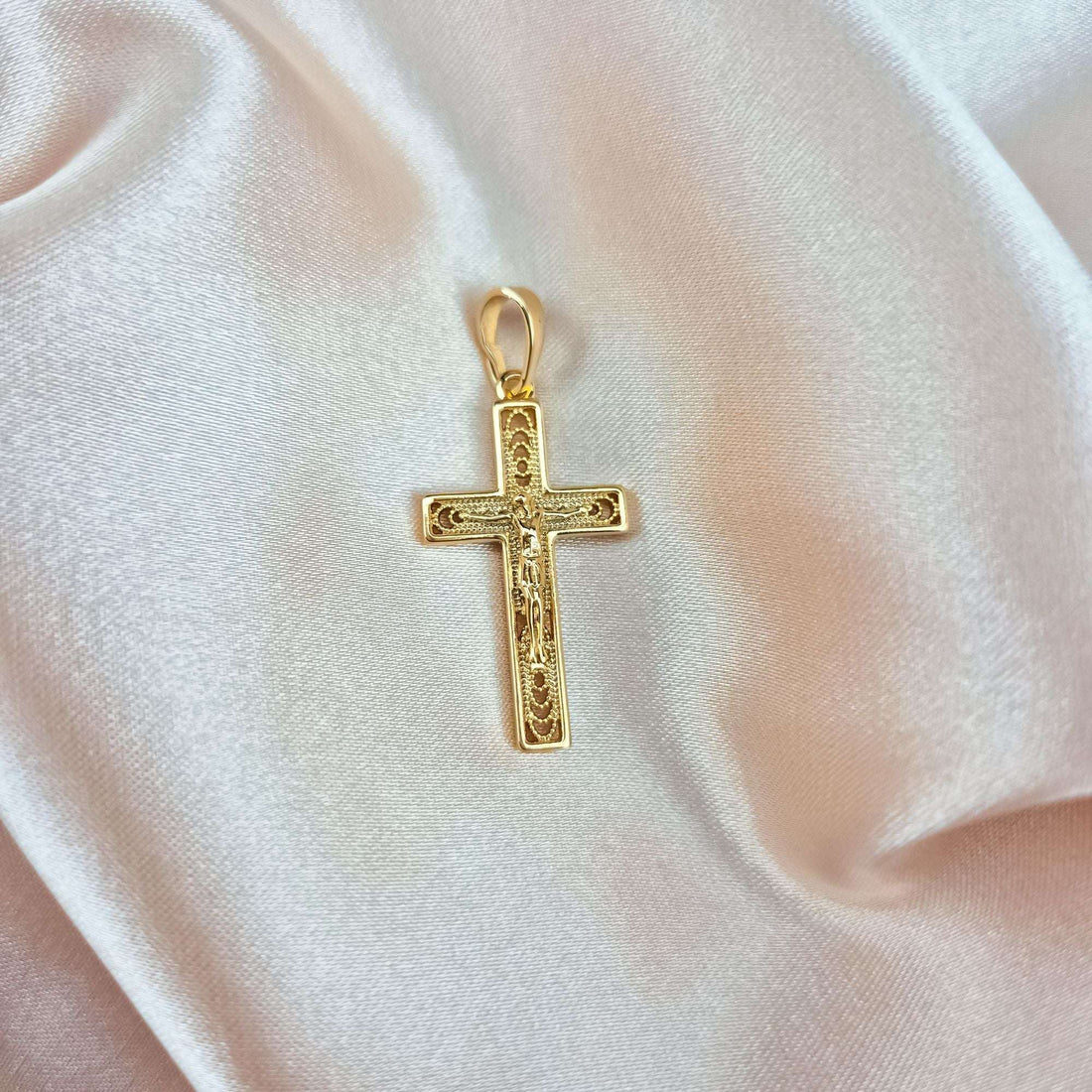 Gold-tone crucifix pendant on cream silk, close-up of the openwork edge