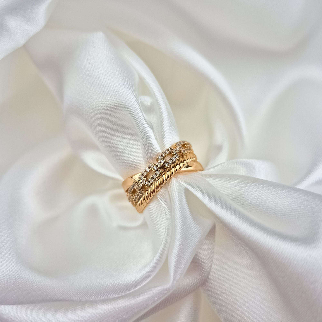 Gold-plated crystal ring on white silk, close-up of the twisted bands