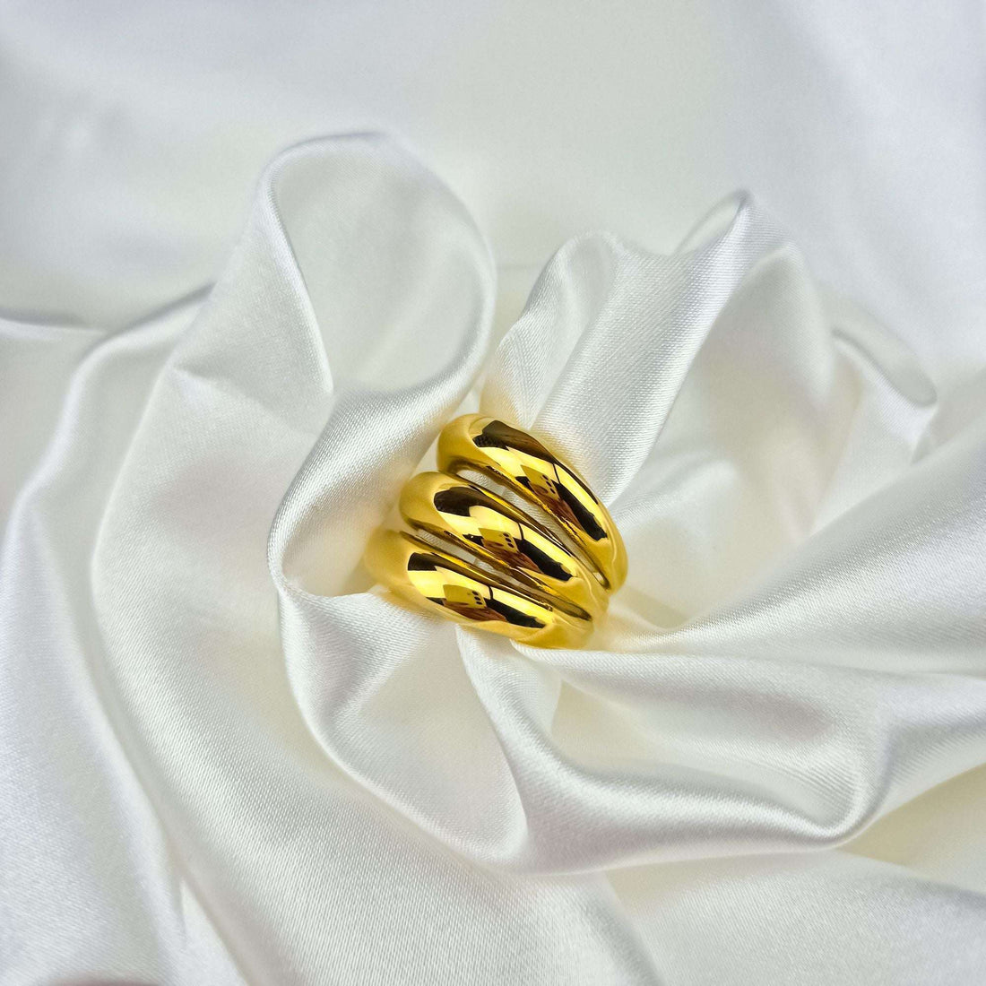 Close-up of a chunky gold-plated wavy ring on white silk folds