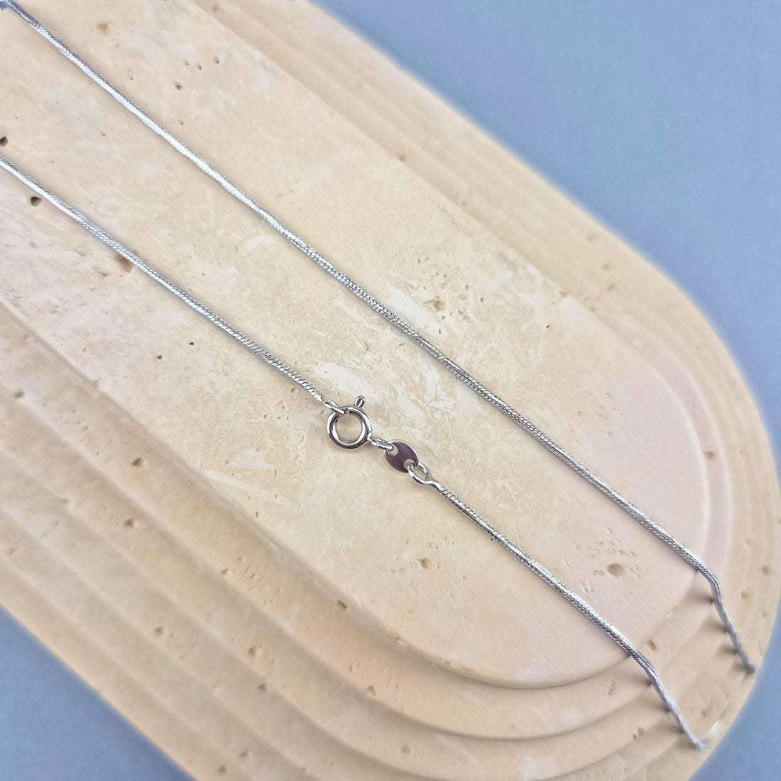 Silver-tone snake chain laid out on a light stone slab, clasp visible