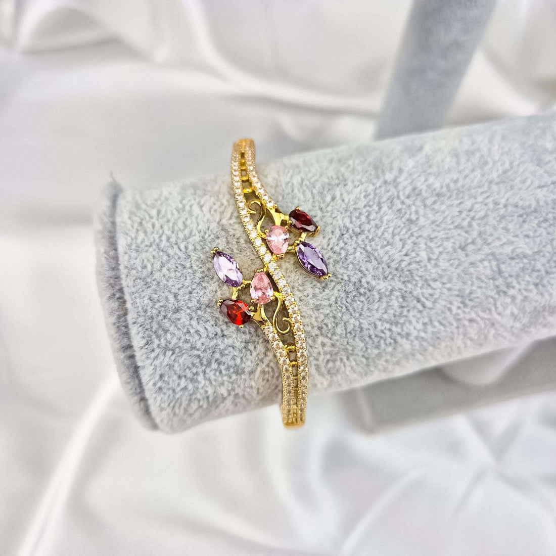 Gold-plated bangle with red, violet and pink cubic zirconia on a jewellery stand