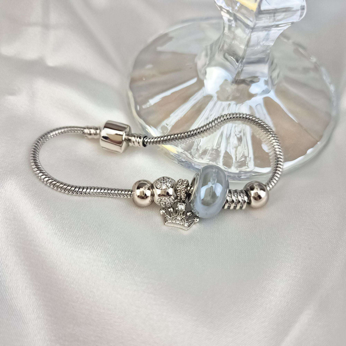 Close-up of the charm bracelet on pale silk, crown charm and pearly bead