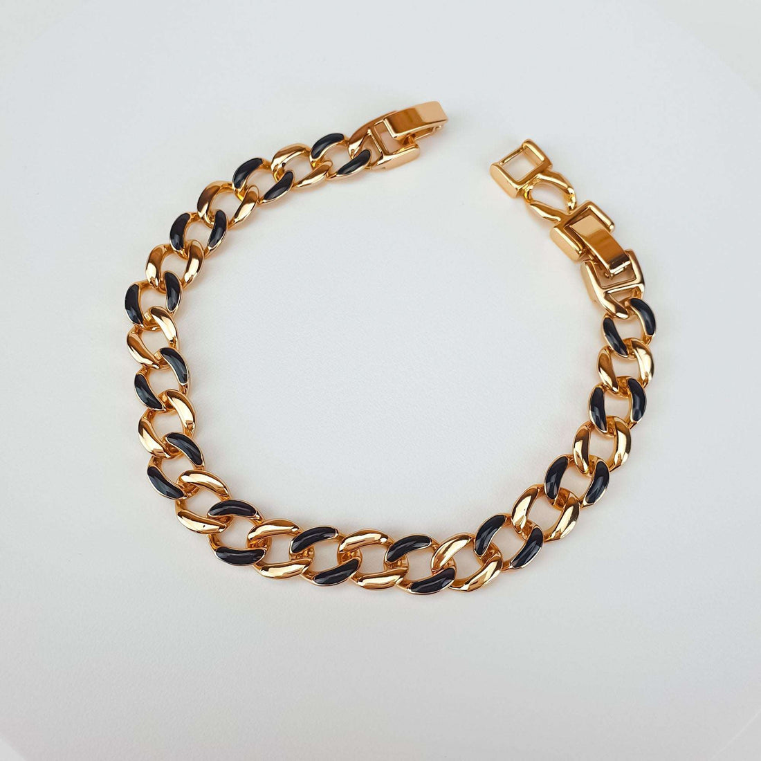 Black enamel and gold-tone bracelet at an angle, with the clasp open