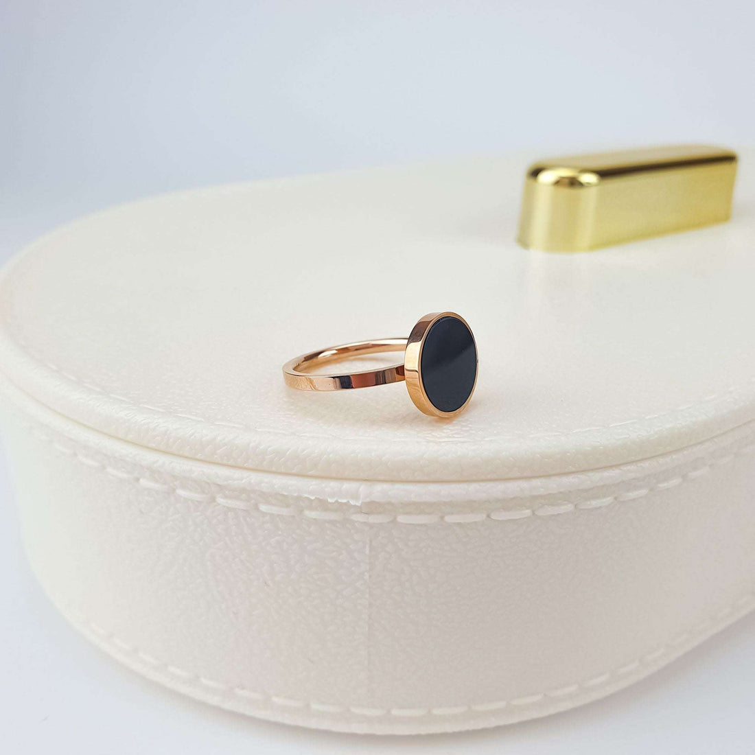 Black accent ring on a cream gift box, side view, warm gold tone