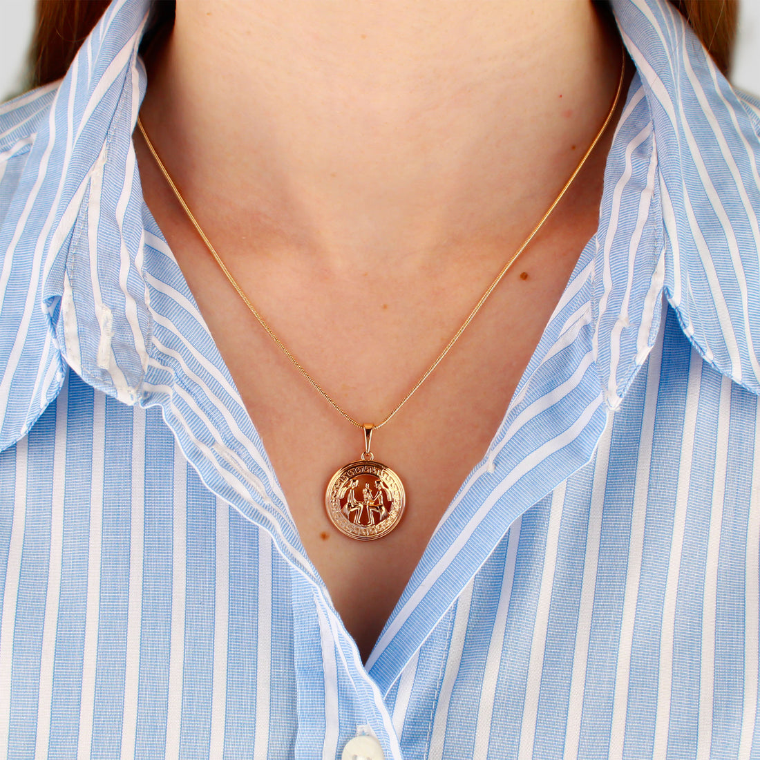 Fine gold-plated chain worn with a round zodiac pendant over a striped shirt