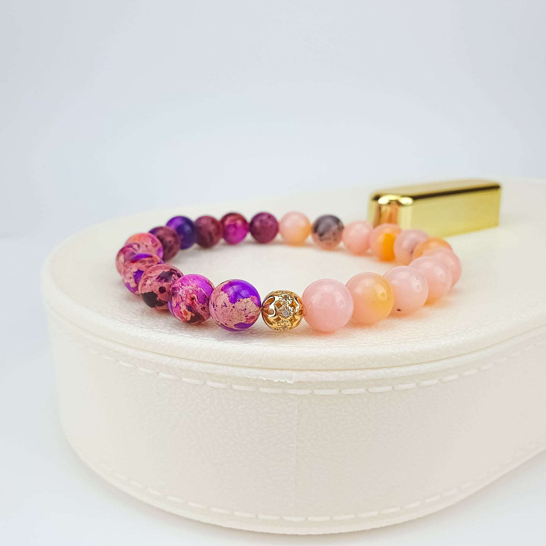 Side view of the bracelet, a gold-tone bead between pink and violet stones