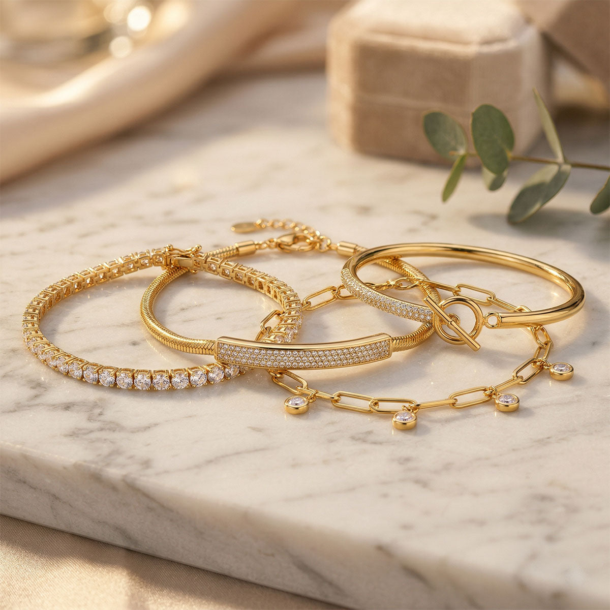 Tennis bracelet, wide cubic zirconia band and smooth bangle, all gold-plated, on marble