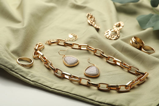 Gold-plated chunky chain, earrings with a pale stone and rings on light green fabric