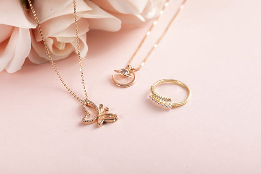 Gold-plated butterfly pendant, fine chain and pearl ring on soft pink background with roses