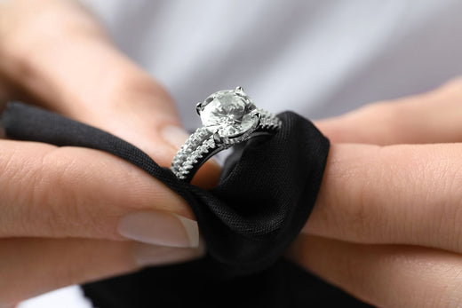 Close-up of hands polishing a large clear cubic zirconia ring with a black cloth