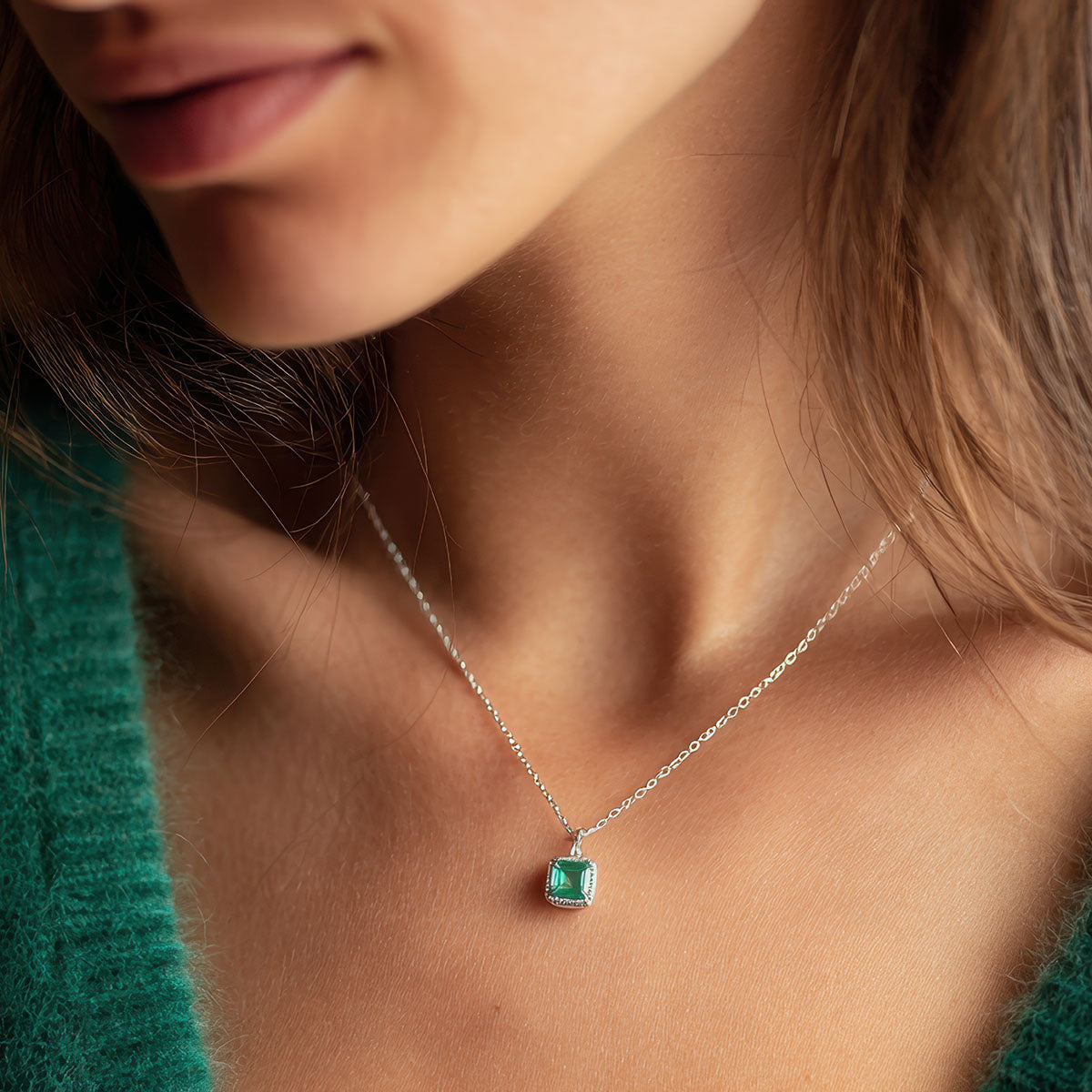 Square green-stone pendant on a silver-tone chain worn with a green knitted jumper