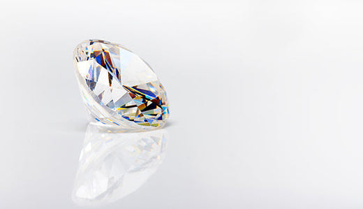 Brilliant-cut clear stone with rainbow reflections on a bright white surface