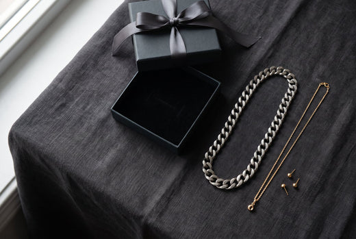 Open gift box, chunky chain, fine chain and bar earrings on a dark windowsill