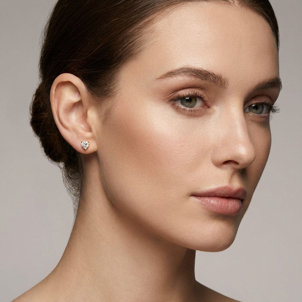 Gold-plated heart stud in a model's ear, side view on a grey background