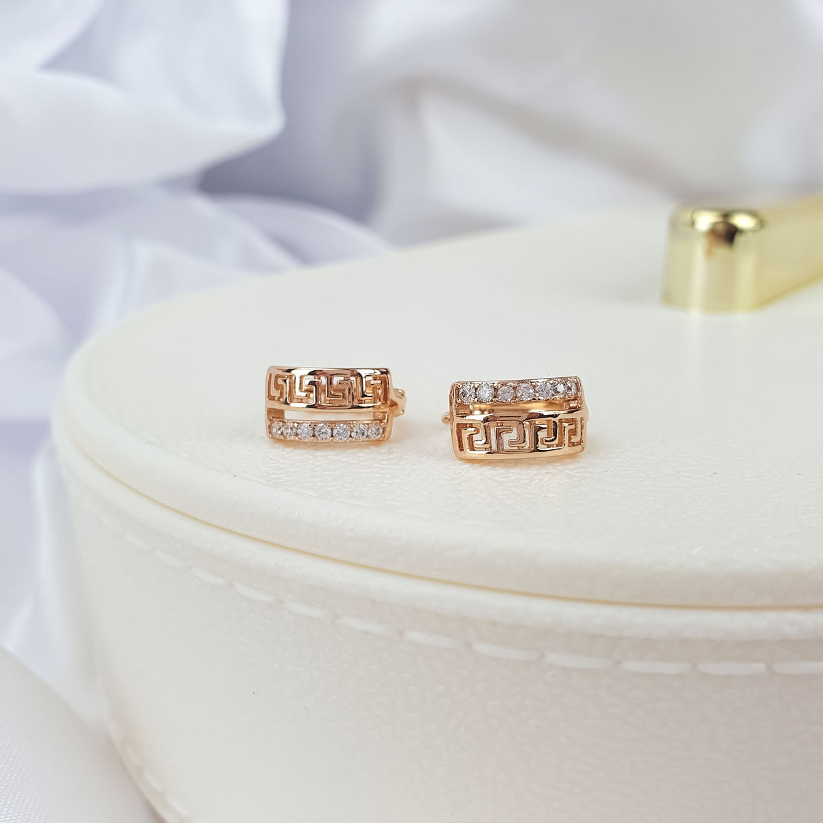 Pair of gold-plated Greek key earrings with cubic zirconia on a cream jewellery box