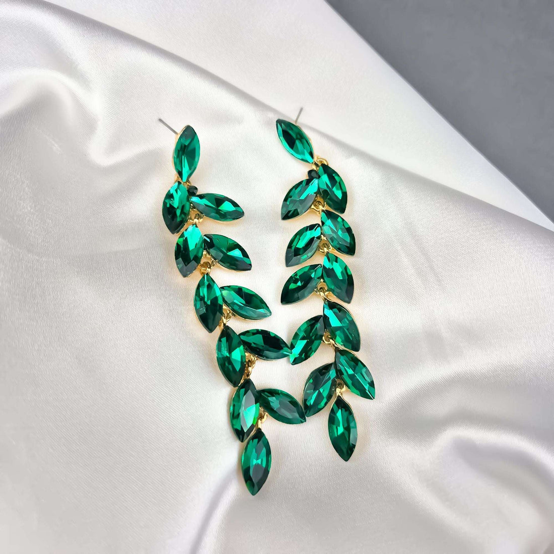 Green crystal leaf earrings on white satin with push-back posts visible