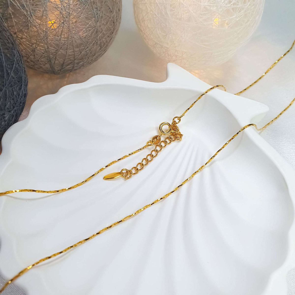 Gold-plated twisted chain with an extender on a white shell-shaped tray