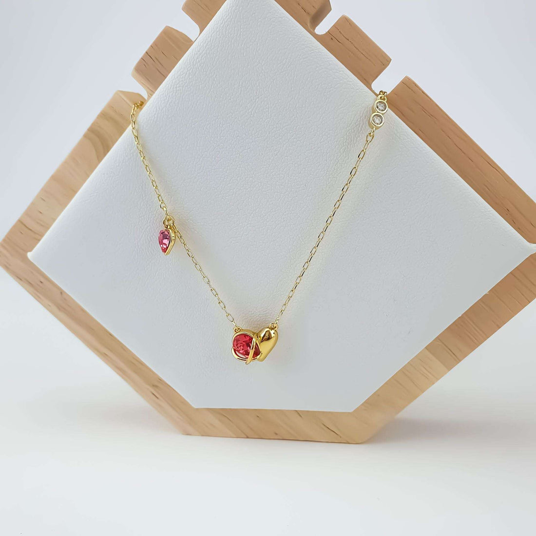 Gold-plated heart necklace with rosy stones displayed on a white jewellery stand