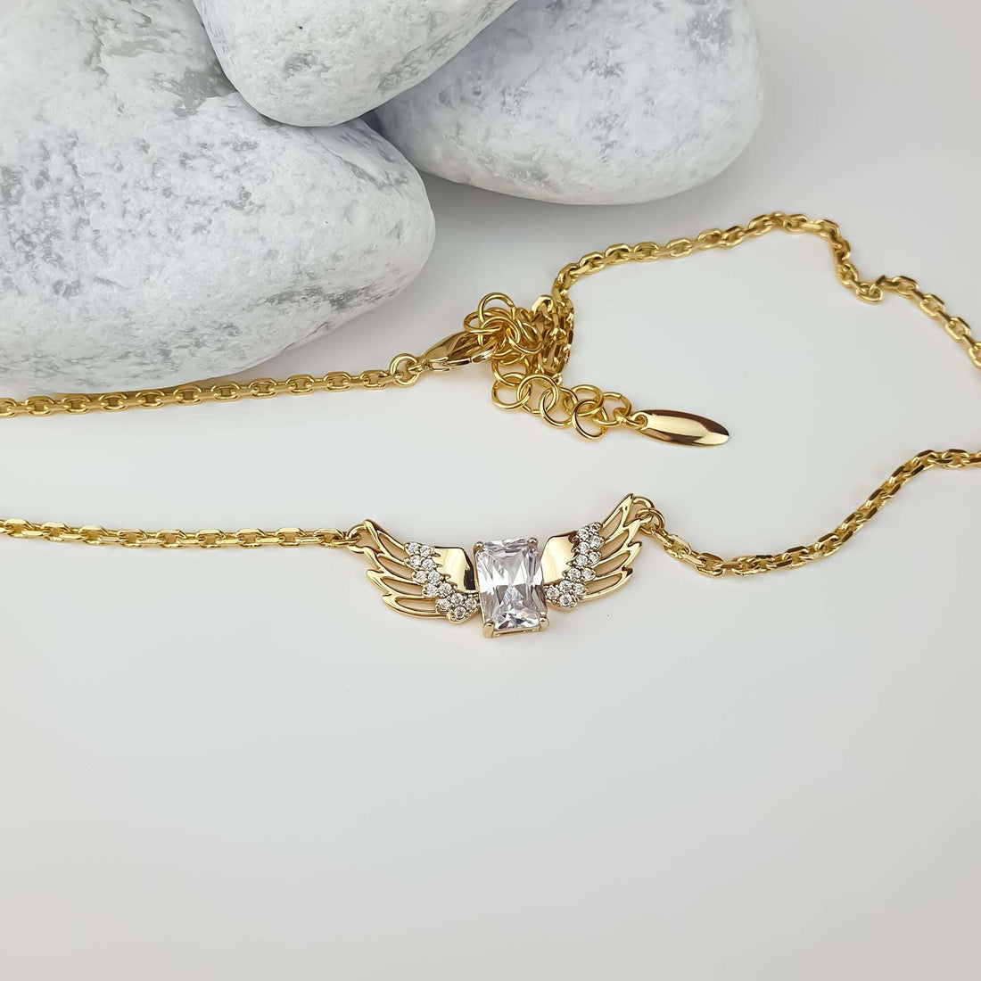 Wing necklace laid beside light stones, showing the clasp and extension chain