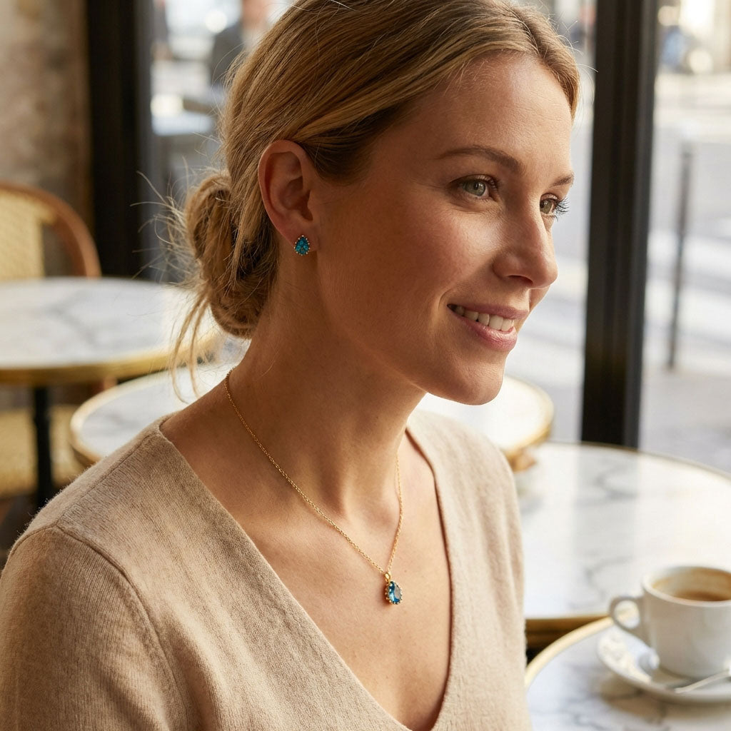 Woman in a café wearing a gold-plated necklace and earrings with blue drops