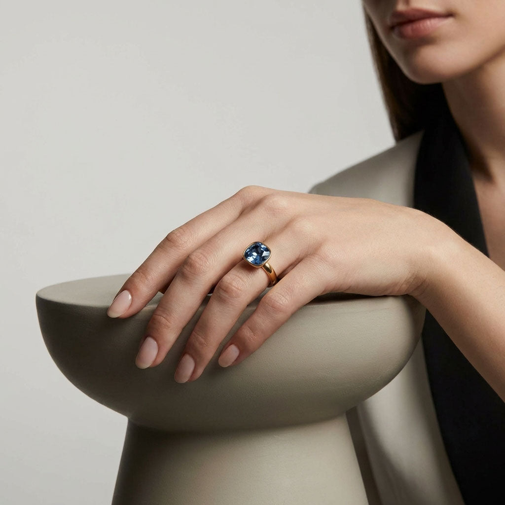 Model wearing the gold-plated blue crystal ring, hand resting on a light plinth