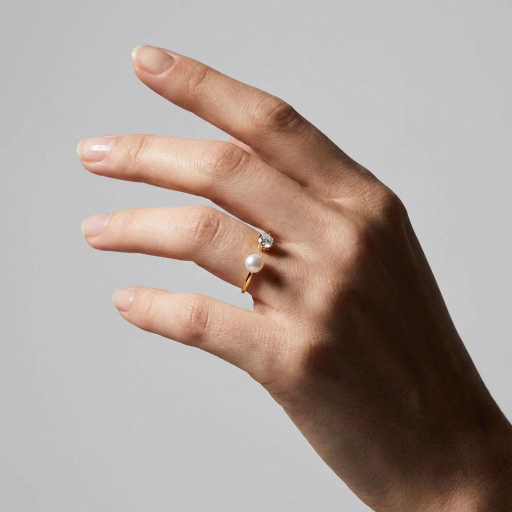 Gold-plated pearl and cubic zirconia ring on a model's finger, grey background