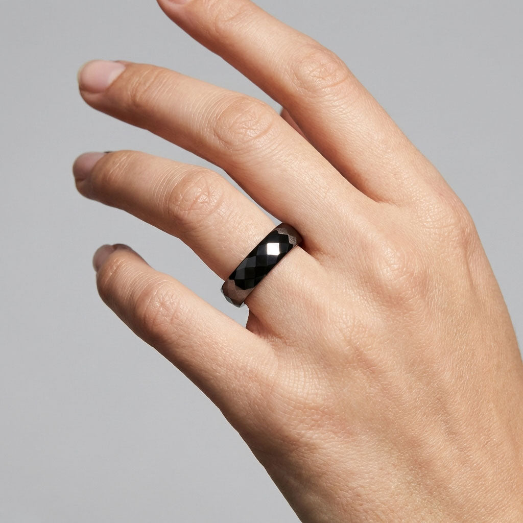 Black ceramic ring with sparkling facets on a man's finger, grey background